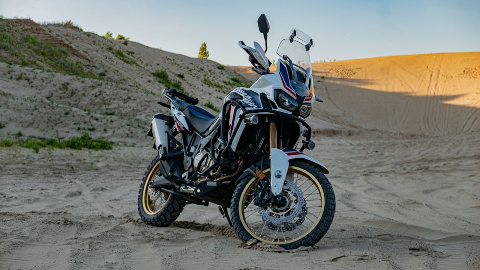 A rugged adventure motorcycle parked on expansive desert sand dunes, captured at daylight