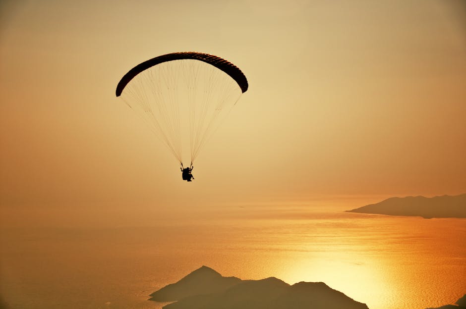 A silhouette of a paraglider flying over the stunning Ölüdeniz at sunset.