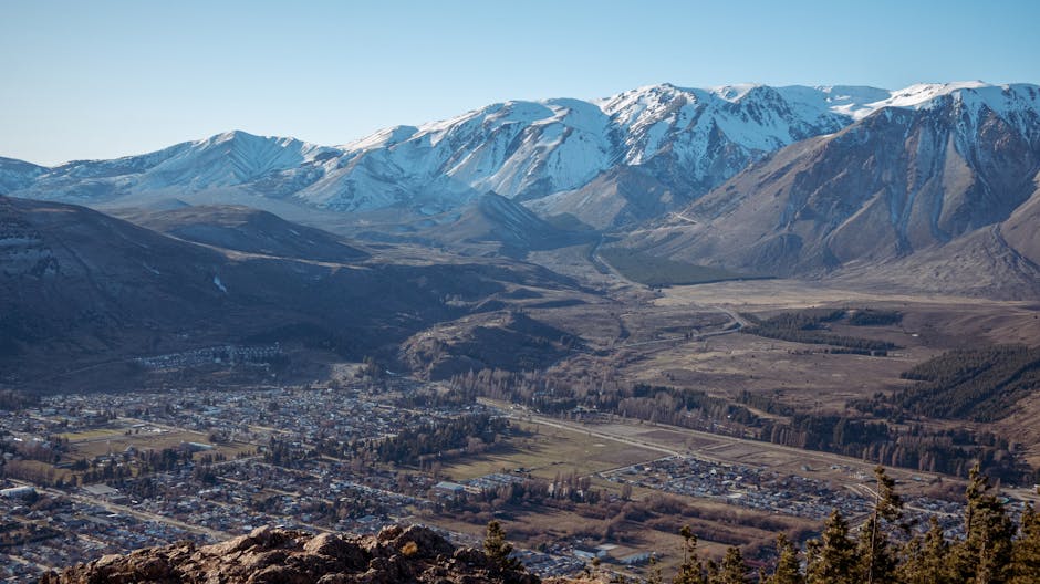 Breathtaking aerial view of a town against snow-capped mountain backdrop under clear blue sky
